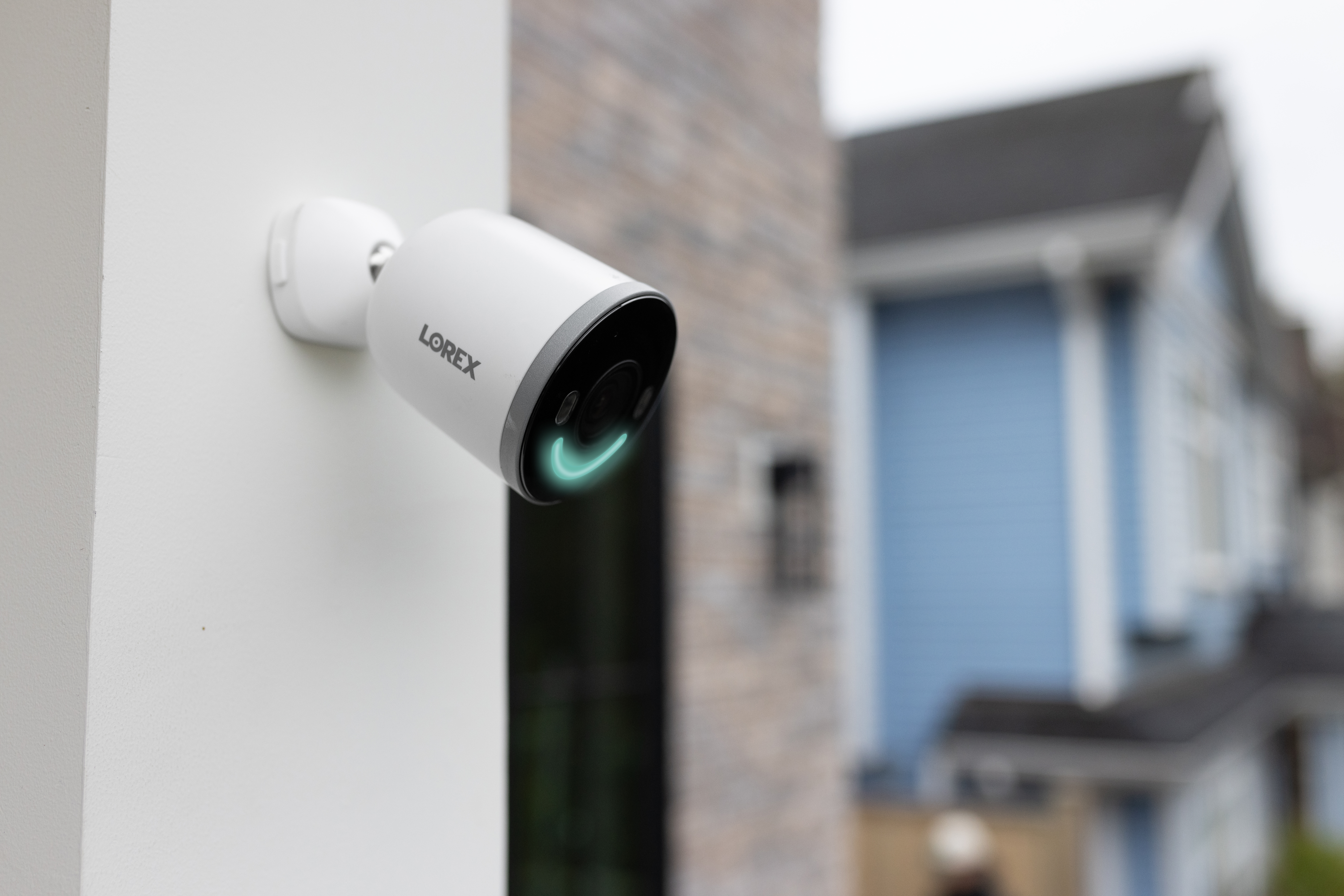 A white Lorex 4K video camera attached to the outside wall of a house.