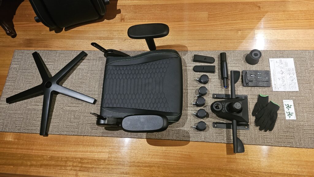 All parts of the chair have been laid out and ready to assembly alongside the tools and gloves that were provided. There's the chair base, chair, wheels, adjustments, stickers, and small version of instructions