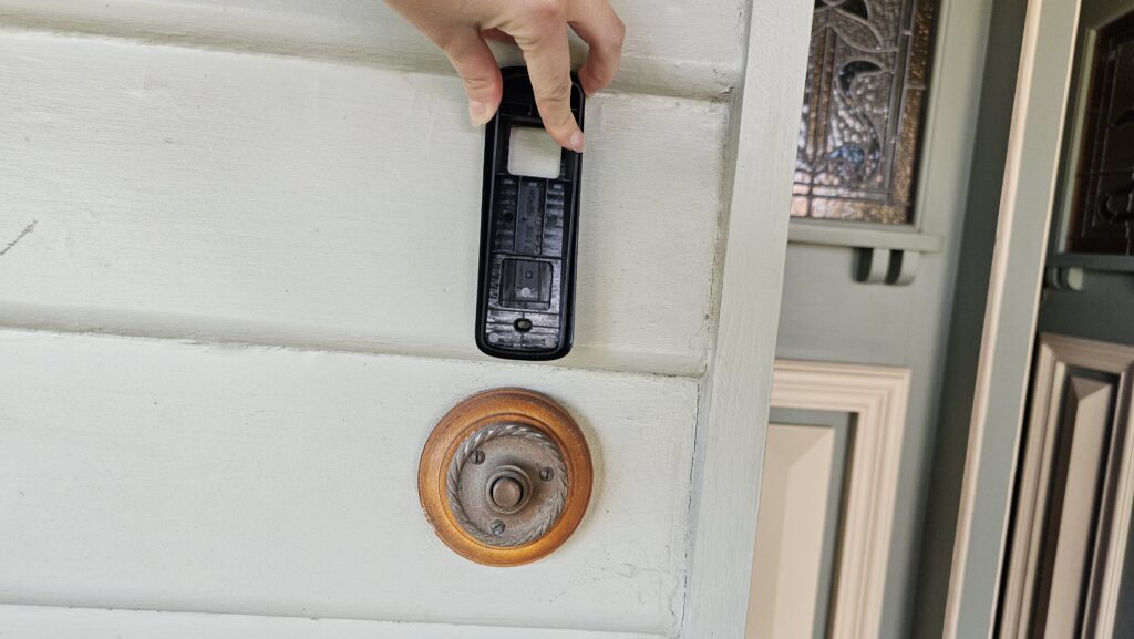 Black mounting bracket sitting against a light green panel and above an antique looking doorbell.