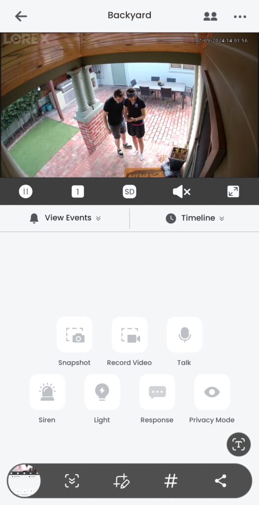 Live view page showing "Backyard" an image of two people looking down at a phone, and there's a few buttons on the screen showing "snapshot, record view, talk, siren, light, response, and privacy mode".