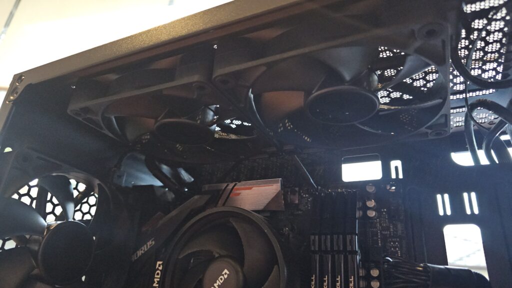 Inside of a PC. You can see the Motherboard, ram sticks, and three fans. Everything is black.